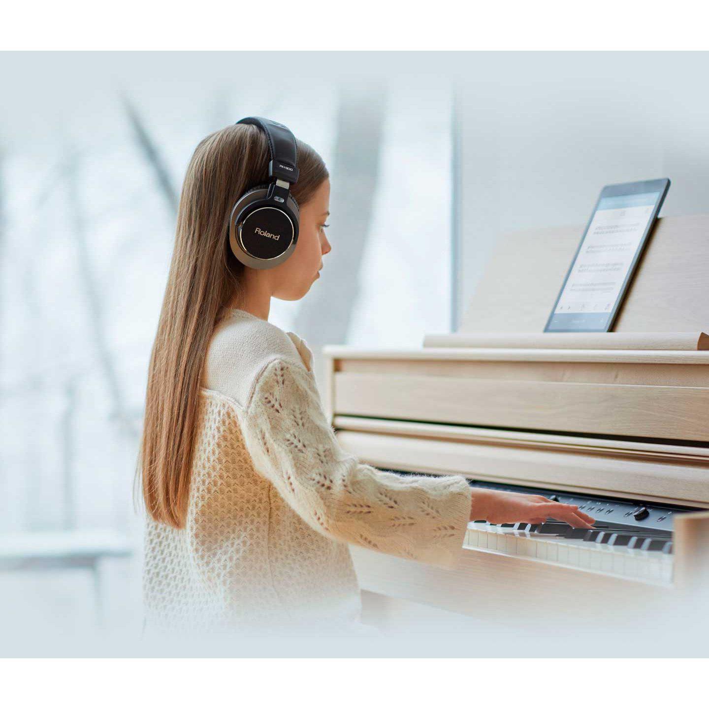 Ung pige med høretelefoner spiller digitalpiano i lyst rum med nodeblad på bordet.