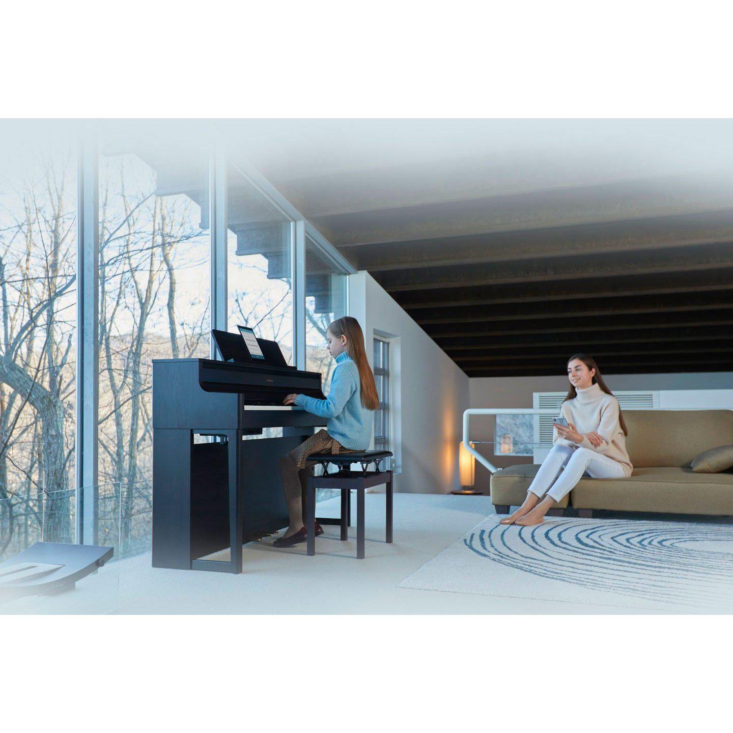 Sort digitalpiano i moderne stue med ung pige, der spiller, og kvinde der ser på.