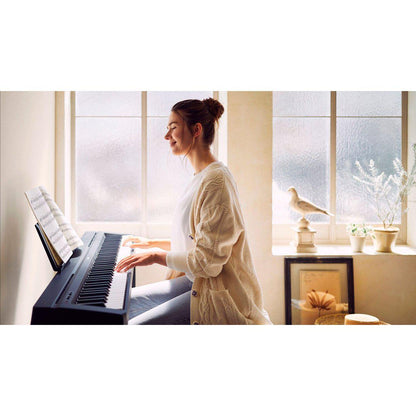 Kvinde spiller på sort Yamaha stagepiano ved vindue med naturligt lys, noter på stander og beige bluse.
