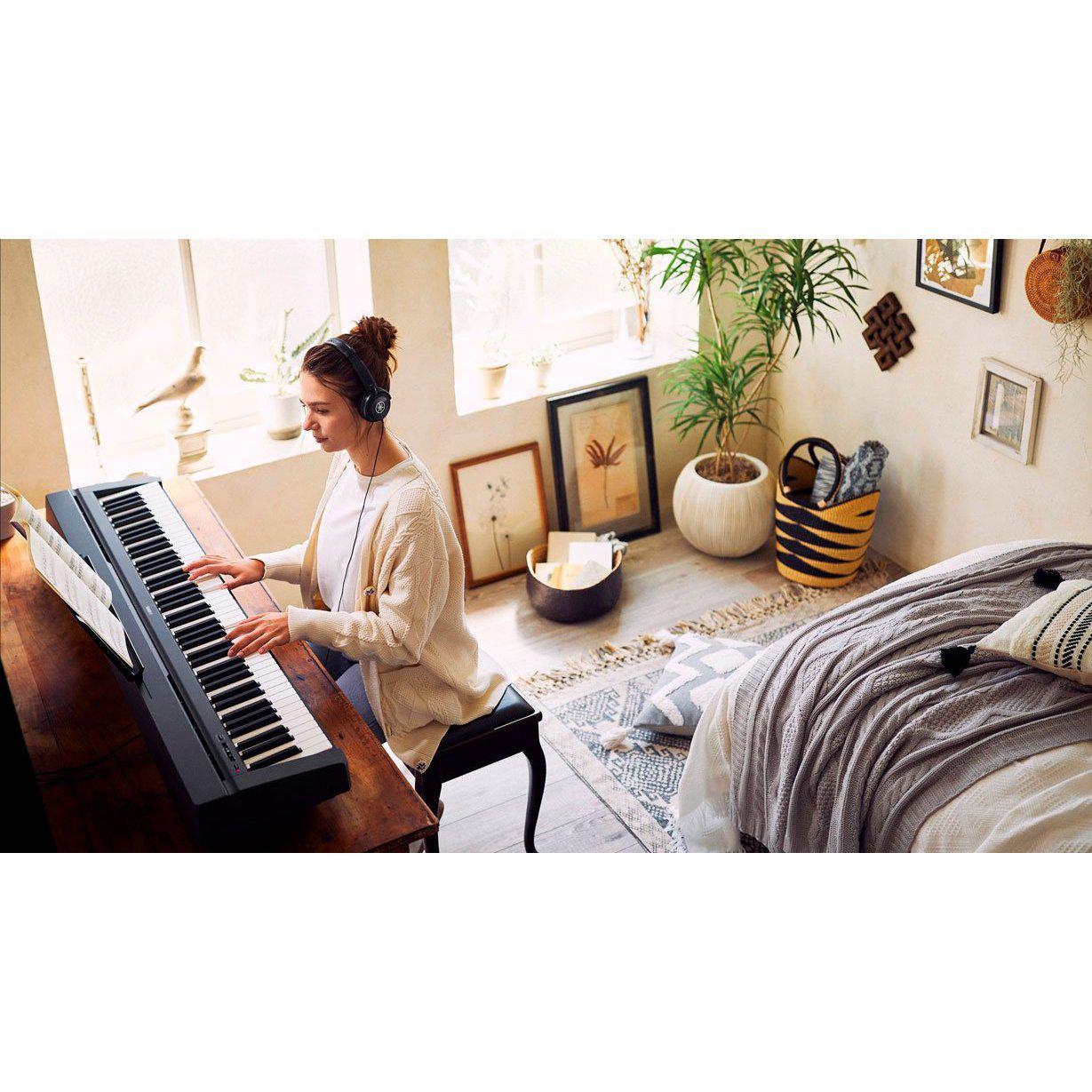 Sort Yamaha stagepiano med 88 tangenter, placeret ved vindue i lyst værelse med kvinde der spiller keyboard, grønt plante,.