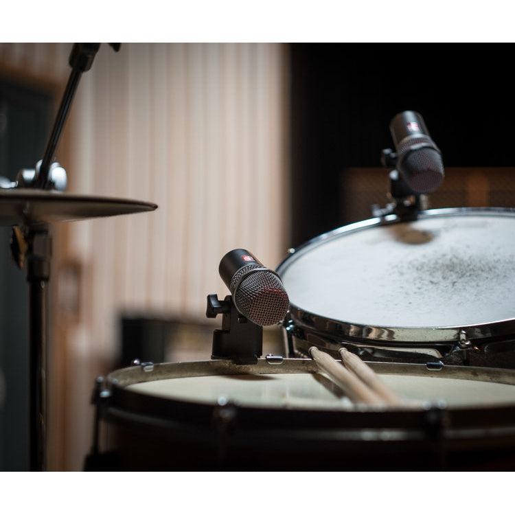Dynamisk mikrofon monteret på trommer i musikstudie med trommestikker ved siden af.